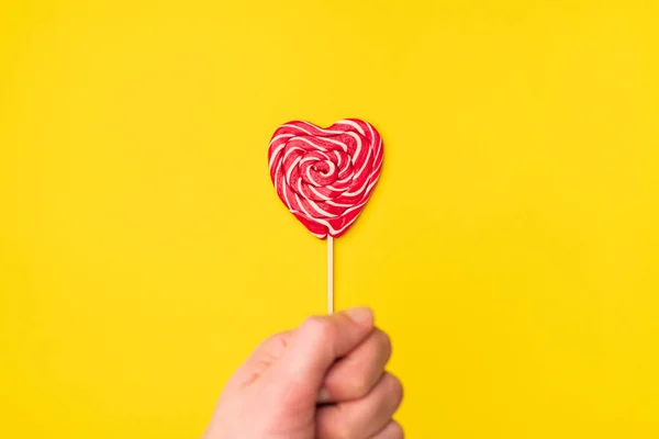Elleri kırmızı kalp şeklindeki lolipop şekeri boş sarı bir arka planda izole edilmiş. Mutlu Kadınlar Günü 'nün, Sevgililer Günü' nün, doğum günü kartpostalının aşk sembolü. Düz konum, üst görünüm, kopyalama alanı