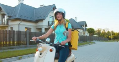 Teslimat servisinden beyaz güzel bir bayan işçi. Termal sırt çantalı bir kaskla. Neşeli genç kadın kurye scooter 'da oturuyor, bakıyor, gülümsüyor ve kameraya başparmak işareti yapıyor..
