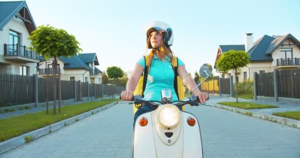 Porträt einer attraktiven kaukasischen Kurierin, die auf einem Roller fährt und Lebensmittel ausliefert. Hübsche junge Zustellerin auf der Suche nach der richtigen Adresse. E-Commerce, sicherer Online-Einkauf im Internet. — Stockvideo