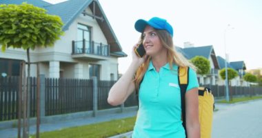 Sırt çantalı neşeli beyaz kadın kurye yemek siparişi veriyor. Güzel kadın teslimat işçisi ev adresi için müşteriyle konuşuyor. Salgın sırasında online alışveriş.