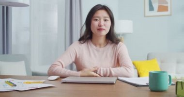 Ofis odasındaki masada oturan kendine güvenen Asyalı kadın. Giyim kuşamında gamzeleri olan güzel bir kız öğrenci kameraya bakıyor ve gülümsüyor. Modern minimalist tasarım.