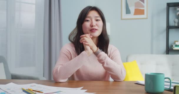 Mujer asiática bastante joven sentada a la mesa en la habitación minimalista moderna en casa. Sonriente vlogger mujer está hablando con la cámara, haciendo conferencia en vivo, grabación de blog. Redes sociales, vlogging. — Vídeos de Stock