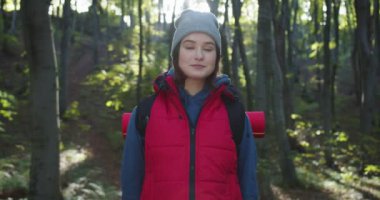 Ormanda durup gün ışığına gülümseyen genç ve güzel bir kadın yürüyüşçüye yakından bakın. Yürüyüş, orman, aktivite, gençlik, tatil, doğada seyahat eden insanlar. Vahşi Yaşamda Yolculuk