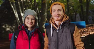 Ormanda gülümseyen genç ve güzel bir çiftin portresi. Renkli şapkalı kadın ve erkek turist orman manzarasına bakıyor. Doğada seyahat eden insanlar kavramı.