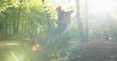 Yakışıklı bir erkek sırt çantasının yaz ormanlarında akıllı telefonuyla oturup, internette gezinerek, sohbet ederek, kayarak, mesajlaşarak rahatlayacağı bir plan. Seyahat yaşam tarzı konsepti. Ormanda cep telefonu kullanan adam.