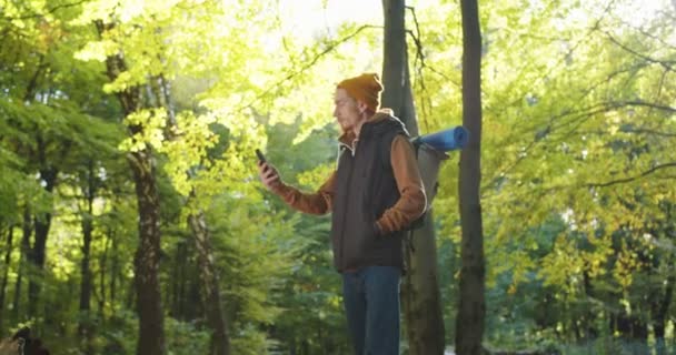 Zbliżenie na młodego podróżnika w kapeluszu, próbującego złapać sygnał komórkowy w lesie, brak zasięgu w telefonie. Mężczyzna turysta na tle leśny krajobraz. Pojęcie osób podróżujących w naturze. — Wideo stockowe