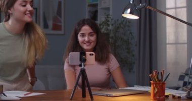 Odada cep telefonuyla görüntülü sohbet ederken gülümseyen güzel beyaz kadın ikizler. Neşeli kız kardeşlerin portresi. Rahat evlerinde akıllı telefondan video görüşmesi yapıyorlar. Boş zaman konsepti