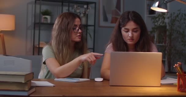 Młode białe bliźniaczki siedzą przy biurku w przytulnym pokoju i uczą się z laptopa. Kobieta przeglądająca komputer i rozmawiająca z siostrą bliźniaczką. Studenci uczą się w domu w zamknięciu. Koncepcja badania — Wideo stockowe