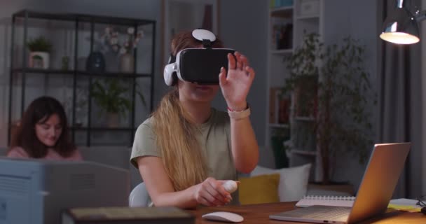 Femme blanche jeune casque VR en utilisant la technologie et faire des gestes dans l'air avec les mains tandis que sœur jumelle sur fond utilise smartphone Portrait de la femme dans des lunettes de réalité virtuelle 3D moderne — Video