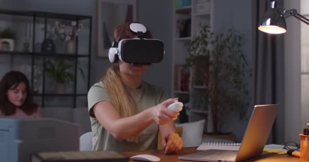Portrait d'une jeune femme caucasienne dans un casque VR utilisant la technologie et faisant des gestes avec les mains tandis que sa sœur jumelle sur fond tapote sur smartphone. Femme en réalité virtuelle lunettes — Video