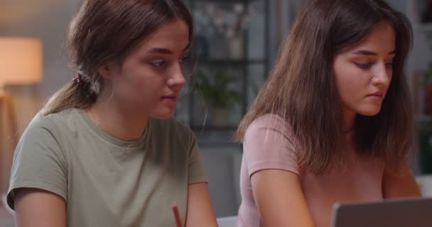 Close up portrait of concentrated beautiful Caucasian twin sisters sitting in room at home and studying with laptops. Pretty young twins students learning at home. Home education concept — Stock Video