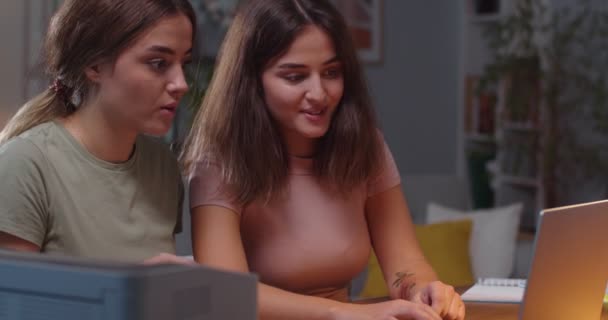 Primer plano retrato de mujeres jóvenes sonrientes alegres sentadas en la habitación en casa y escribiendo en el ordenador portátil mientras ríen y hablan de buen humor. Hermanas gemelas bastante felices navegando en la computadora. Concepto de ocio — Vídeo de stock