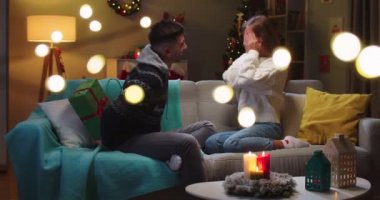 Kanepede oturan mutlu karı-kocanın orta planı. Kapalı gözlerle oturmuş hediye bekleyen bir kız arkadaş. Erkek arkadaşı büyük güzel bir Noel hediyesi veriyor. Aile tatili kavramı.