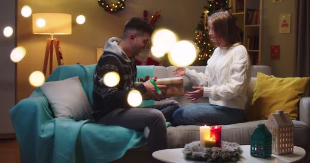 幸福夫妻坐在沙发上的中间计划。女朋友送给男朋友一个大礼品盒.女人把圣诞帽戴在男人身上家庭假日的概念，完美的关系. — 图库视频影像