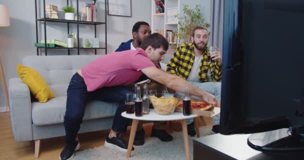 혼합 경주를 즐기는 3 명의 친구들은 집에 모여서 TV 에서 축구 경기 채널이 피자를 먹고 간식을 먹는 것을 보았다. 남자들은 친한 친구들과 즐거운 시간을 보내고 있다 — 비디오