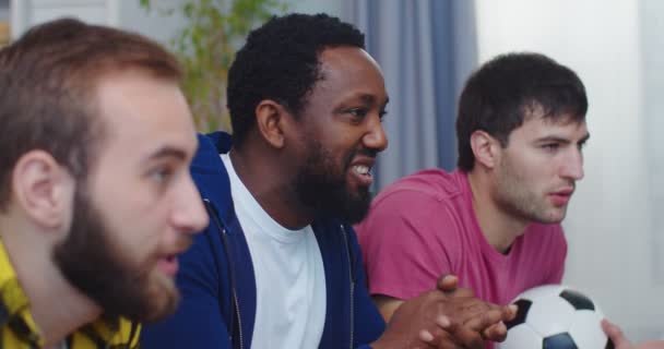 Neşeli, heyecanlı, karışık ırklı erkek en iyi arkadaşlar oturma odasında oturmuş en sevdikleri futbol takımını destekliyor ve spor kanallarını izliyorlar. Gol! Gol! Futbol taraftarları konsepti — Stok video