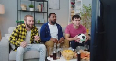Neşeli, mutlu, Afro-Amerikan ve Kafkas erkek arkadaşlar birlikte TV 'de maç izliyorlar. Bağıran, kucaklayan, gol atan ya da zaferi kutlayan erkekler. futbol taraftarları konsepti