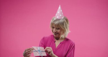Stüdyoda pembe arka planda poz veren, gülümseyen ve elinde şirin zarflı tatil kartı tutan mutlu, son sınıf beyaz kadın portresi. pozitif duygular.