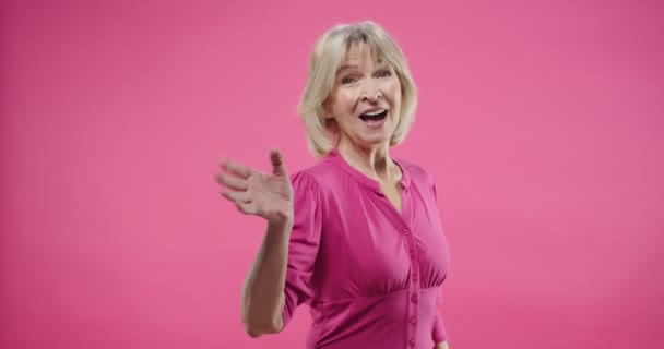 아름다운 연금을 받고 행복 해 하는 백인 여성이 손을 흔들며 인사를 하는 모습과 스튜디오에서 웃음을 짓고 있는 분홍색 배경에 대한 즐거운 표정으로 모두를 환영하는 모습 — 비디오