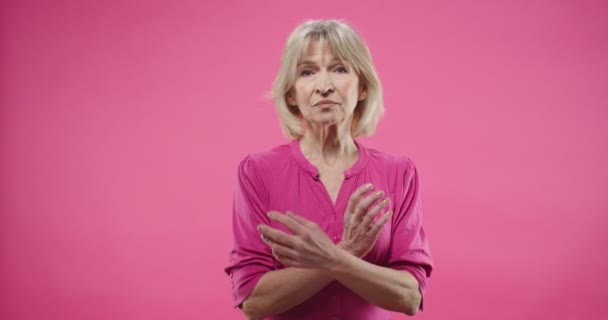 Caucásico ancianos bastante infeliz pensionista mujer bonita con cabello rubio con expresión de cara pretenciosa de pie en el estudio sobre fondo rosa mirando a la cámara no satisfecho. Concepto de retrato. — Vídeo de stock