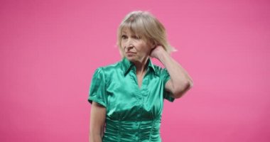 Mutsuz, güzel, beyaz, yeşil bluzlu yaşlı bir kadının portresi. Stüdyoda pembe duvarda yalnız başına, tatminsiz bir yüz ifadesiyle kameraya bakıyor.