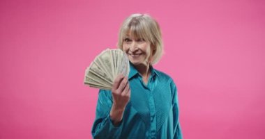 Beyaz son sınıf öğrencisinin portresini yakından çek. Stüdyoda pembe arka planda poz veren oldukça şık, neşeli bir kadın. Keyfi yerindeyken gülümsüyor ve elinde bir sürü dolarla kameraya bakıyor. Para kavramı