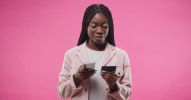 İnternetten alışveriş. Afro-Amerikan genç neşeli güzel kadının portresi cep telefonuyla yazan kredi kartıyla ödeme yapan pembe arka planda duran. E-ticaret kavramı