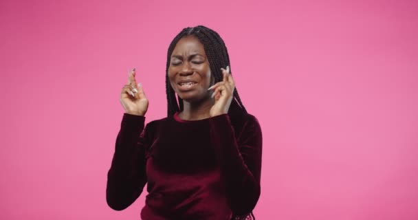 Close-up portret van gelukkige jonge mooie Afro-Amerikaanse vrouw staan op roze rooskleurige achtergrond in de studio wachten op een aantal resultaten met opgewonden bezorgd gezicht en gekruiste vingers bidden voor succes — Stockvideo