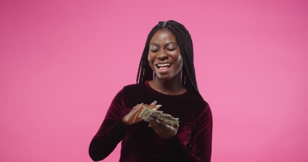 Крупный план портрет счастливой молодой красивой афроамериканской богатой женщины улыбается и бросать доллары держа много денег, стоя изолированы на розовом розовом фоне стены. Концепция бизнеса — стоковое видео