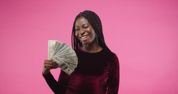 Portrait de jeune femme brune afro-américaine assez joyeuse souriante et regardant la caméra tout en posant sur un mur de fond rose tenant de nombreux dollars à la main avec un visage heureux. concept d'argent — Video