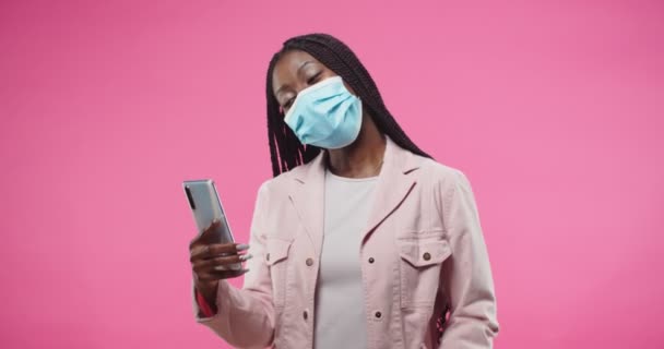 Πορτρέτο της Αφρικής Αμερικανός νεαρή χαρούμενη όμορφη γυναίκα σε βίντεο μάσκα στο smartphone μιλάμε για βιντεοκλήση στο διαδίκτυο στέκεται σε ροζ φόντο στο στούντιο. Ψυχαγωγική έννοια. online chat — Αρχείο Βίντεο