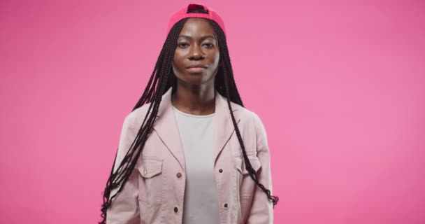 Portrait of African American young pretty cheerful woman wearing red cap in positive mood smiling and making OK gestures with fingers approving with hand posing isolated on rosy background in studio — Stock Video