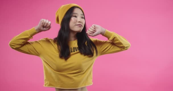 Portrait de heureuse jeune belle asiatique positive femelle en chapeau jaune jouissant de danser sur la musique mains en mouvement rythmiquement isolé sur fond rose rosé. Drôle de danse. Concept de loisirs — Video