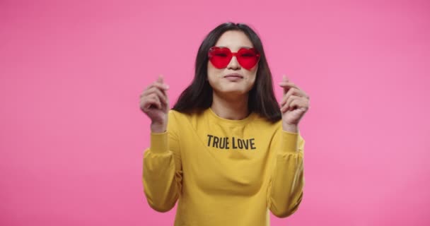 Portrait de belle asiatique joyeuse femme heureuse portant des lunettes modernes élégantes rouges debout seul isolé sur fond rose faisant des gestes de coeur et des mouvements drôles avec les mains, concept d'émotions — Video