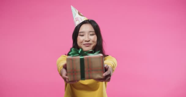 Retrato de la hermosa mujer joven alegre asiática en sombrero de cumpleaños celebración de b-day caja de regalo en las manos de pie en el estudio sobre fondo rosa en el estado de ánimo positivo. Celebración. Concepto actual — Vídeos de Stock