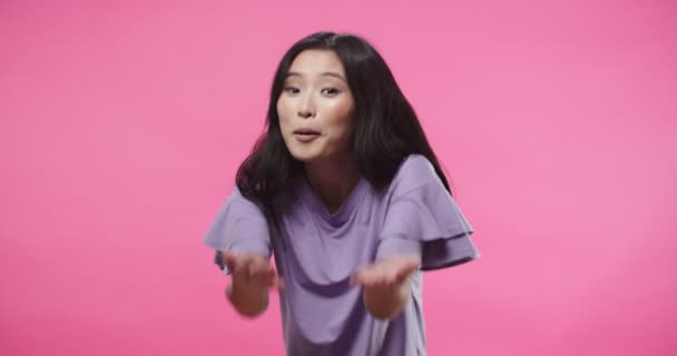 Porträt von fröhlich glücklich freundlich schöne asiatische Frau lächelnd und jemanden anrufen, während er in die Kamera schaut, die im Studio auf rosa Hintergrund steht, selbstbewusste Frau, die zum Kommen einlädt, positive Emotionen — Stockvideo
