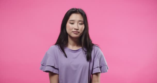 Nahaufnahme Porträt einer glücklichen hübschen jungen asiatischen Frau in lila Bluse, die isoliert auf rosa Hintergrund im Studio steht und in die Kamera mit einem Lächeln auf dem Gesicht in positiver Stimmung blickt. — Stockvideo