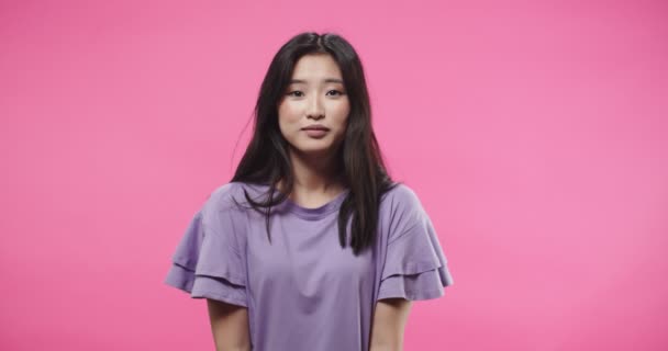 Nahaufnahme Porträt einer fröhlichen schönen jungen Asiatin in lila Bluse, die isoliert auf rosa Hintergrund im Studio steht, spricht und gut gelaunt in die Kamera lacht. Emotionales Konzept — Stockvideo
