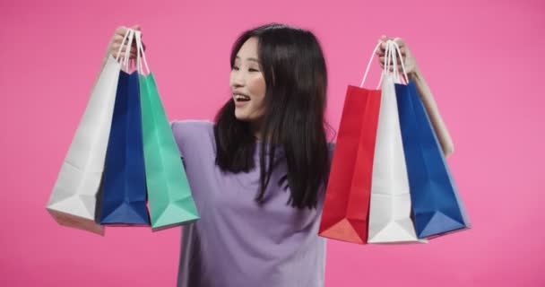 Retrato de feliz jovem asiática segurando muitos sacos de compras em mãos mostrando suas compras para câmera e sorrindo com expressão facial satisfeita. Comprando coisas, conceito shopaholic — Vídeo de Stock