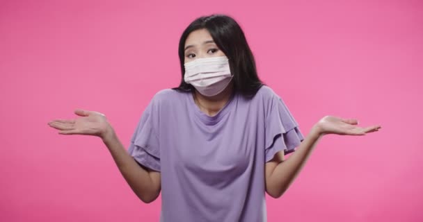 Портрет невпевненої азіатської вродливої жінки в масці поширюючи руки в жестах допиту, дивлячись спантеличеним, не знає, як пояснити, спантеличено поширює руки і килими. — стокове відео