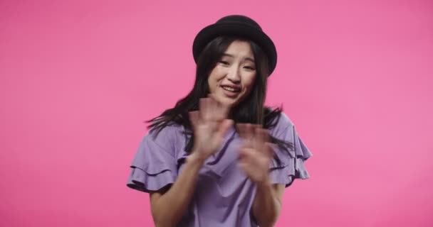 Крупным планом портрет счастливой красивой азиатки в черной шляпе, стоящей изолированно на розовом фоне и спрашивающей меня, отрицающей и отвергающей что-то, указывающей пальцем на кого-то или что-то — стоковое видео