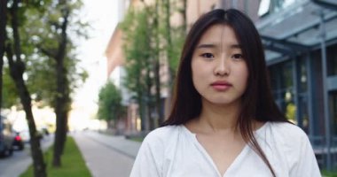 Resmi kıyafetli gülümseyen Asyalı genç kadın sokakta kameraya bakıyor. Mutlu iş kadını portresi işi. Güzel modern menajer.