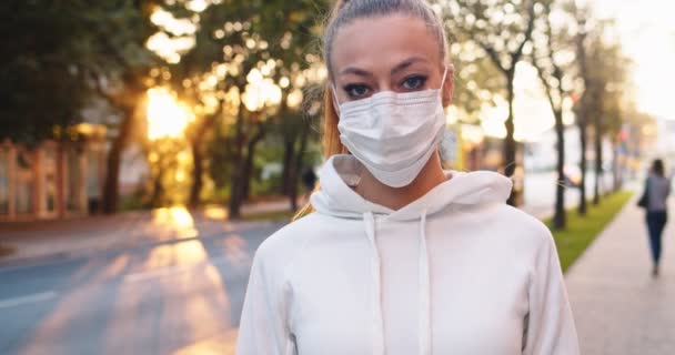 Portret pewnej siebie atletki w odzieży sportowej stojącej na chodniku w parku. Młoda biała kobieta w masce medycznej patrząca na kamerę na ulicy. Covid-19, zdrowie, koncepcja koronawirusa. — Wideo stockowe