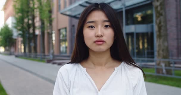 Усміхнена азіатська молода жінка в офіційному вбранні, дивлячись на камеру на вулиці, відчуває себе щасливою бізнес-леді портретний бізнес красивий сучасний менеджер досить повільний рух — стокове відео
