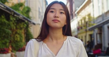 Genç bir kadın kameraya bakıyor. Sokak şehri yaşam tarzında çekici, güzel bir saç standı. Açık hava, doğal yavaş çekim.