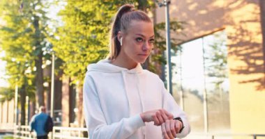 Spor giyim sektöründe kendine güvenen bayan sporcu kronometre kullanarak zaman zaman koşu sonuçları alıyor. Kulaklıklı genç beyaz kadın müzik dinliyor, akıllı saati dinliyor ve şehir sokaklarında koşuyor..