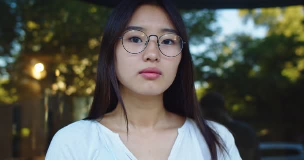 Portret atrakcyjnej azjatyckiej bizneswoman patrzącej w kamerę i zakładającej okulary. Dorosła kobieta pracująca na ulicy miejskiej. Zawód, koncepcja pracy. Tło parku. — Wideo stockowe