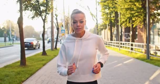 Forte atleta femminile che si allena, facendo jogging per mantenersi in forma nella strada urbana della città. Donna caucasica adulta con auricolari che corrono lungo alti edifici per uffici moderni e ascoltano musica. Concetto sportivo. — Video Stock