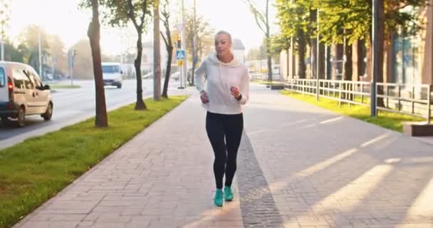 Beyaz kadın spor kıyafetleriyle caddede kardiyo antrenmanı yaparken ön planda. Yetişkin bayan sporcu, koşuyor, maraton yarışmasından önce antrenman yapıyor. Sağlık, başarı konsepti. — Stok video