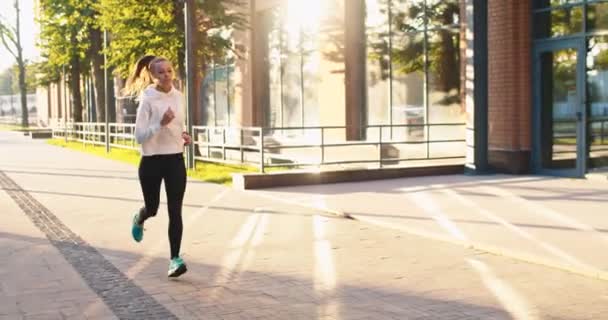 Mooie vrouwelijke atleet in sportkleding opwarmen, trainen om fit te blijven in de stad straat. Volwassen blanke vrouw joggen langs zakelijke gebouwen in de ochtend. Succes gezonde en welvarende levensstijl concept. — Stockvideo